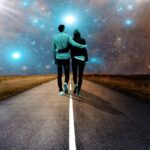 A man and a woman walking together hugging in the middle of the road.