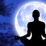 A woman sitting in a yoga position in front of a bright full moon manifesting with the law of attraction.