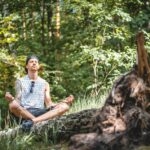 A young man is practicing meditation on a tree log in a calm Berlin forest.