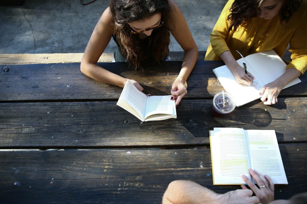 students outside at a picnic table reading books on the law of attraction